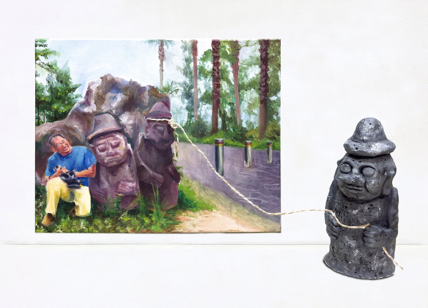 Painting of a man resting beside Jeju stone statues, tied by string to a small sculpted stone figure